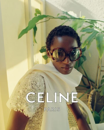 Model with short cropped hair wearing oversized round tortoiseshell sunglasses and a beaded white top with draped scarf in Celine campaign.
