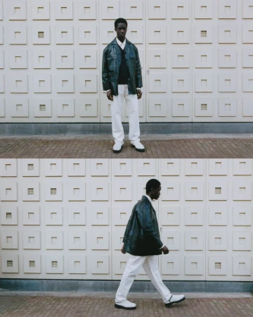 Dark-skinned man in an overshirt, sweater, and white pants poses against a textured wall in full and side profile views, outdoors.