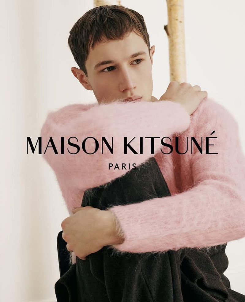 Young male model wearing a fuzzy pink sweater and dark trousers against a white seamless backdrop.