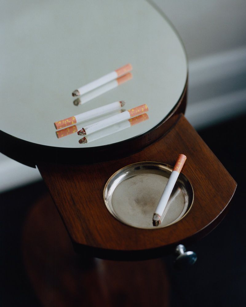 Cigarettes resting on a round vanity mirror stand and pull-out wooden tray with an inset metal ashtray.