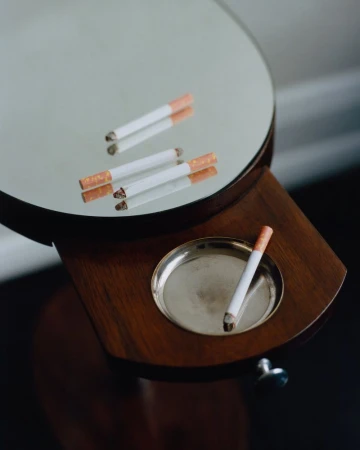 Cigarettes resting on a round vanity mirror stand and pull-out wooden tray with an inset metal ashtray.