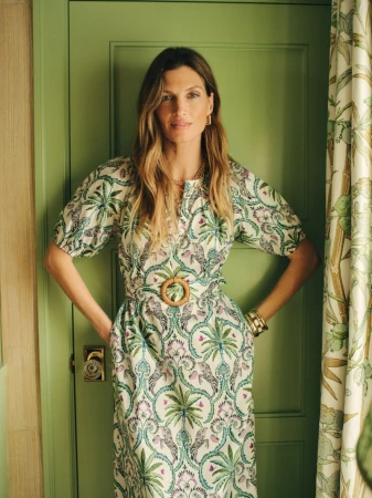 Woman wearing a green and white patterned belted midi dress standing in front of a green paneled door.