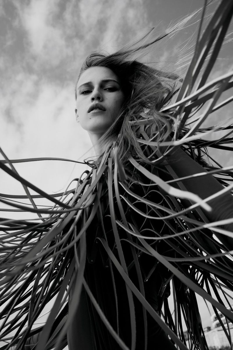 Low angle black and white portrait of model Liva Been wearing an avant-garde fringed garment against the open sky.