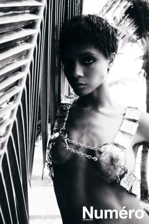 Black and white editorial photo of model Larissa Joseph in a metallic chain bra top posed beside palm fronds.