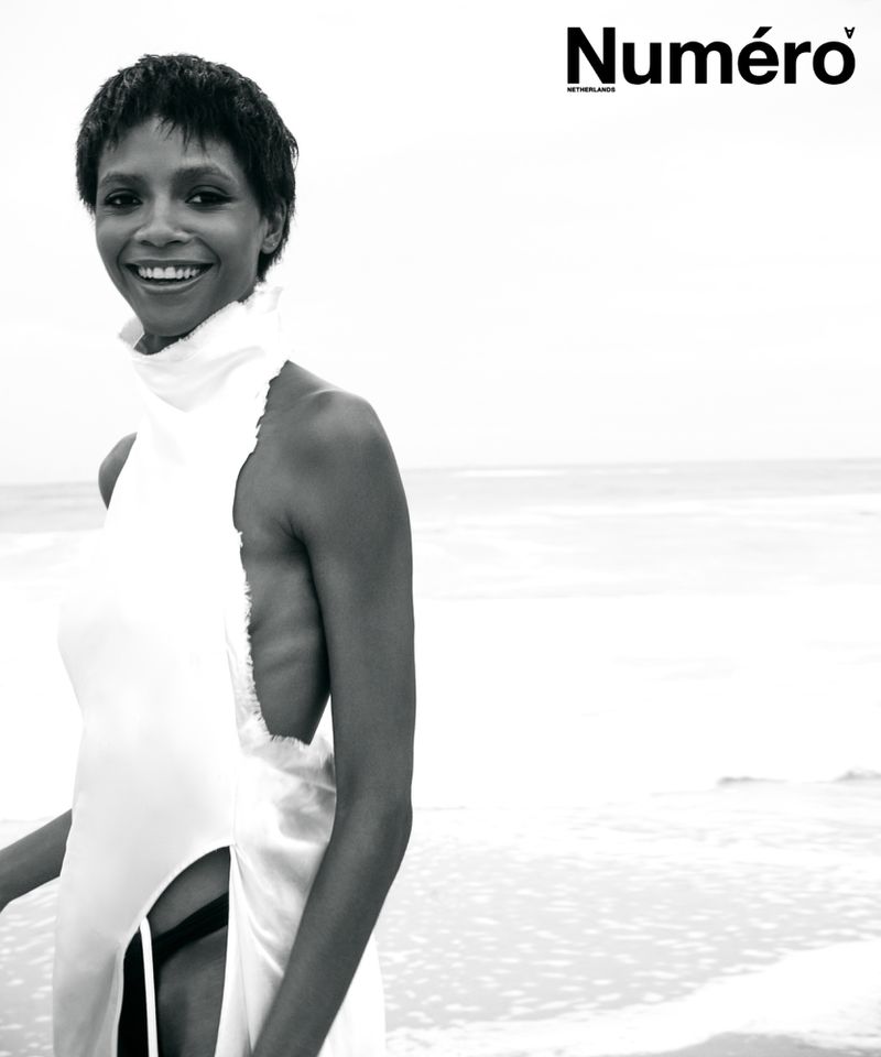 Larissa Joseph poses smiling on a beach in a white sleeveless high-neck garment in black and white for Numéro Netherlands.