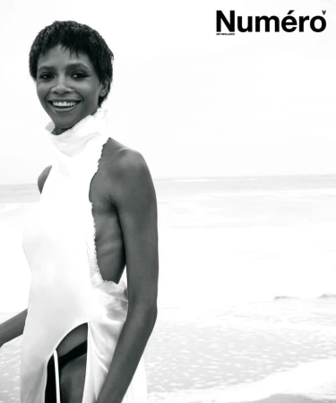 Larissa Joseph poses smiling on a beach in a white sleeveless high-neck garment in black and white for Numéro Netherlands.