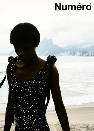 Model Larissa Joseph in a black sequined dress standing on a misty sandy beach with coastal mountains for Numéro Netherlands.