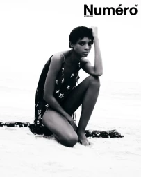 Larissa Joseph crouching on a sandy beach in a star-patterned black dress for Numéro Netherlands.