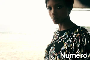 Model Larissa Joseph in an embellished black fringe top looking at the camera outdoors near a bright beach.