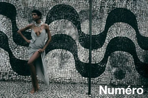 Model Larissa Joseph wearing a draped slip dress and layered necklace posing in front of a monochromatic wave mosaic wall.
