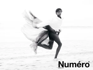 Larissa Joseph leaps along a sandy beach wearing a flowing draped garment in black and white for Numéro Netherlands.