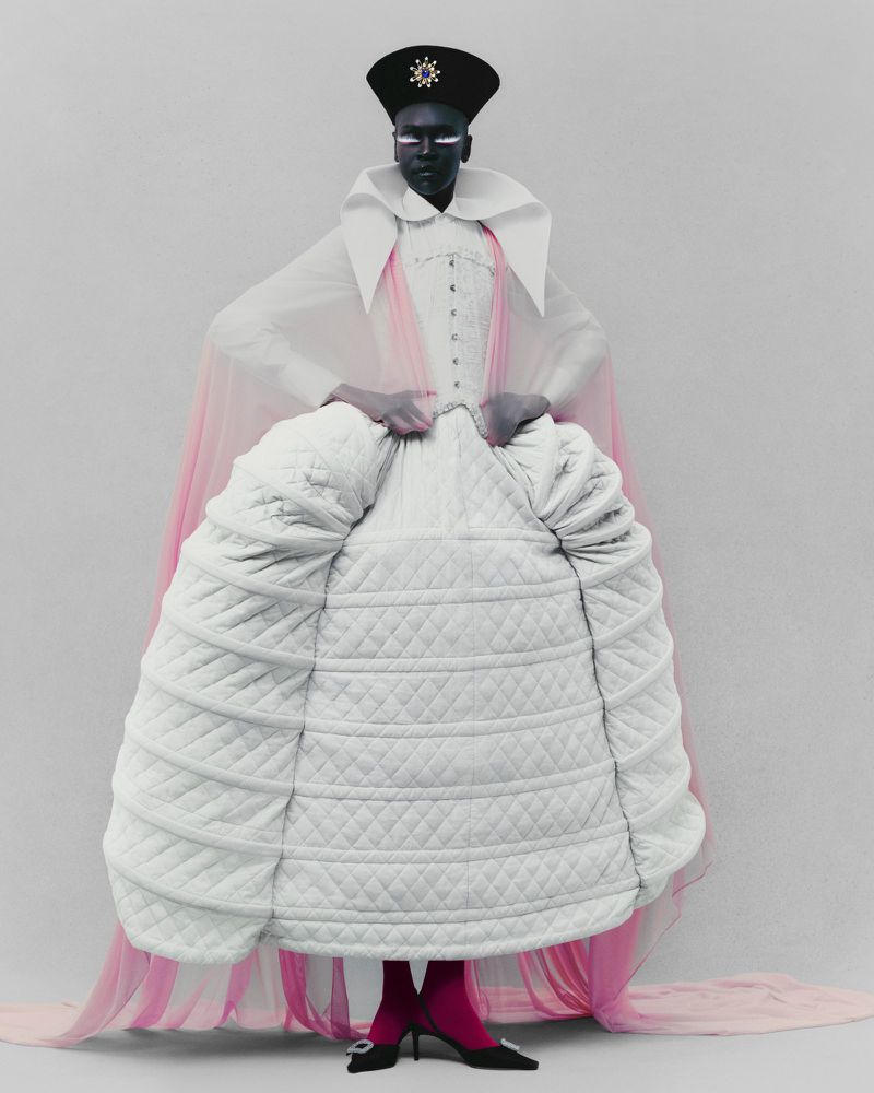A striking fashion image features a model in a unique white quilted dress, a structural collar, and a black cap against a pale backdrop.