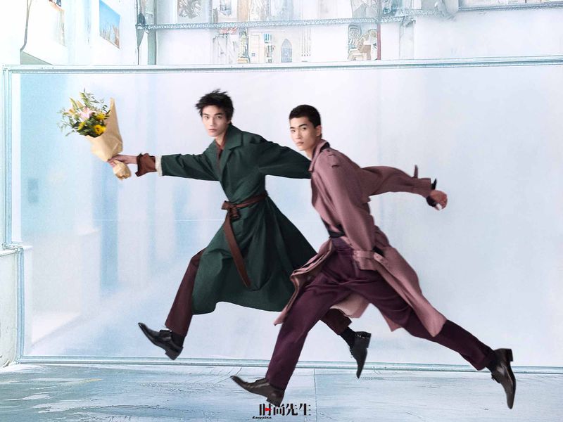 Two male models in trench coats running past a white wall, one holding a bouquet of flowers for Esquire China.