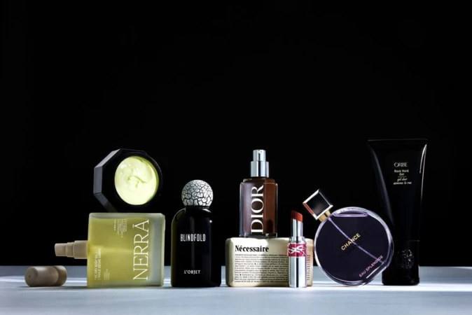 Assorted luxury skincare, perfume bottles, and cosmetic products lined up on a reflective surface against a solid black background.