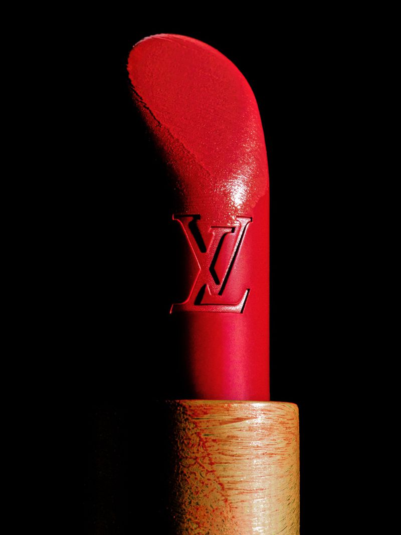 Close-up of a vibrant red lipstick embossed with an LV monogram set in a light wooden casing against a black backdrop.