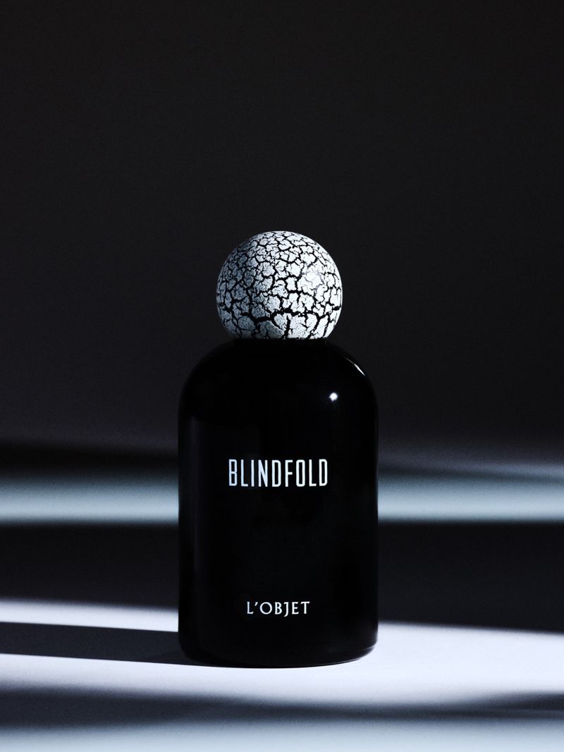L'Objet Blindfold black perfume bottle with a textured crackle sphere cap on a lit surface.