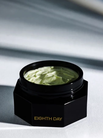 Open black hexagonal jar of Eighth Day face cream revealing textured pale green moisturizer against a neutral background.