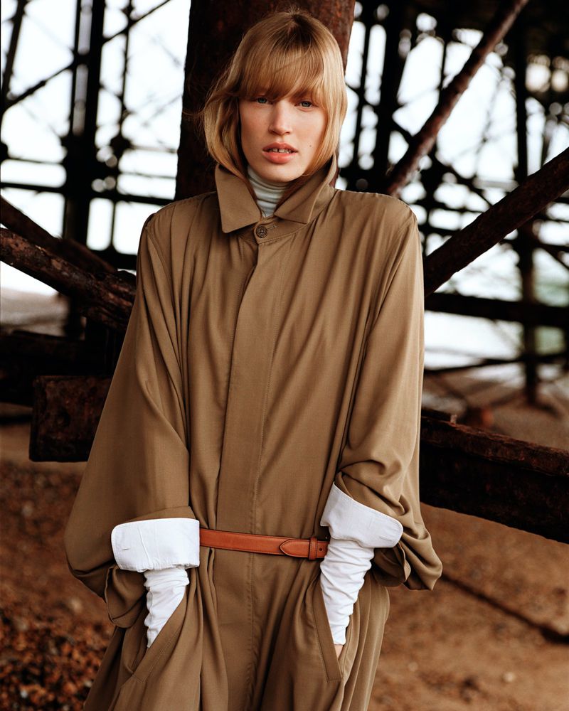 Model Jacqui Hooper in a brown belted coat under a pier structure for Mastermind Magazine, photographed by Alasdair McLellan.