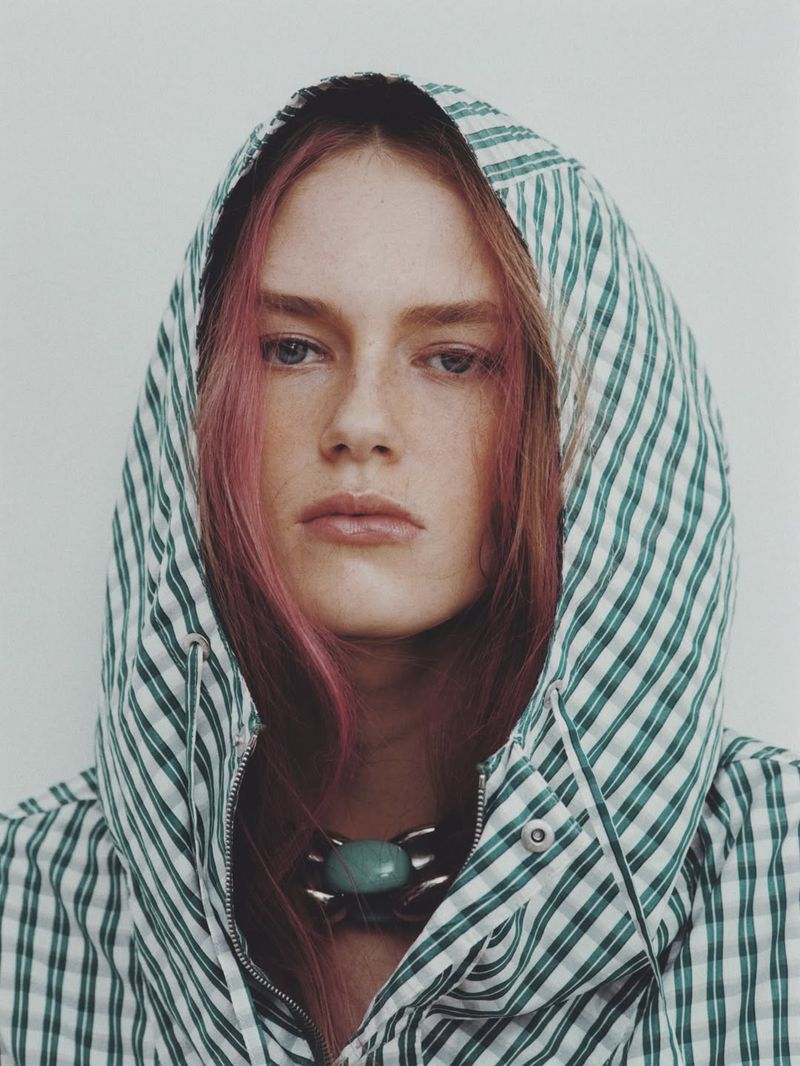 Model Agnes Wahlström wearing a green and white striped hooded jacket with a turquoise necklace against a plain white background.