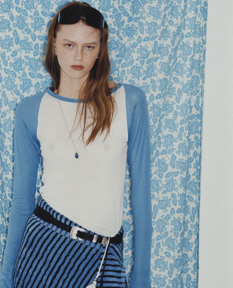 Model Agnes Wahlström wearing a blue and white raglan shirt and striped skirt against a blue floral curtain for Heroine Magazine.