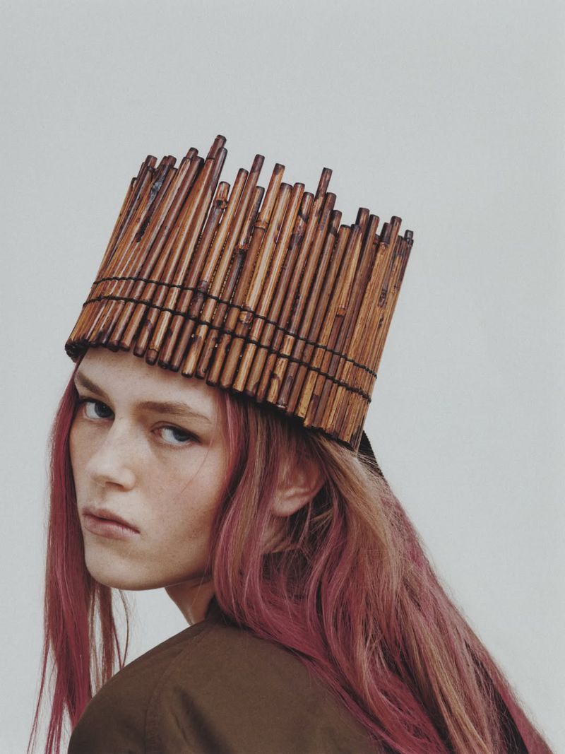 Model Agnes Wahlström wears a cylindrical bamboo stick crown with pink hair against an off-white seamless background.