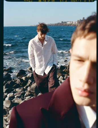 Two male models on a rocky coastline, one in a white striped shirt and one in a burgundy jacket for ICON Magazine Italy.