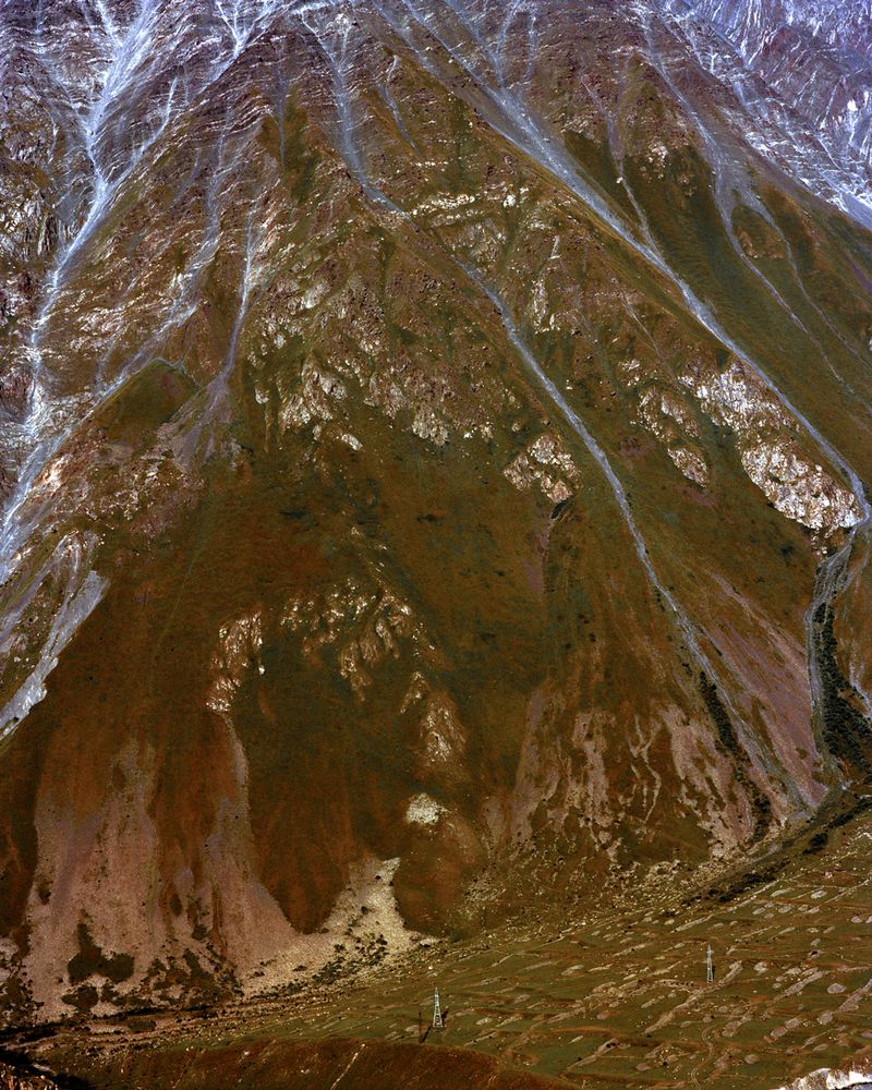 Steep rugged mountain slope with rocky ridges, scree, and patches of snow captured from a high vantage point.