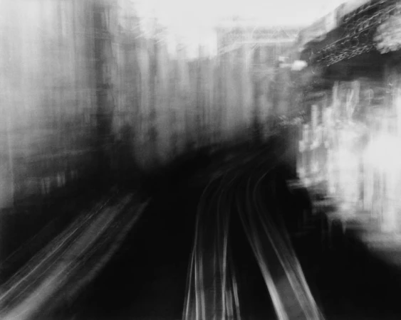 Monochrome abstract motion blur photograph of curving train tracks flanked by blurred city architecture.
