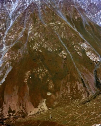 Steep rugged mountain slope with rocky ridges, scree, and patches of snow captured from a high vantage point.