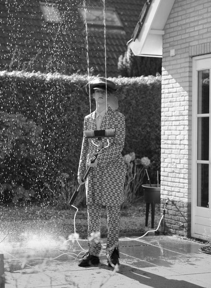 Model Jelle Huizinga in a patterned suit holding a water-spraying window brush on a suburban patio in black and white.