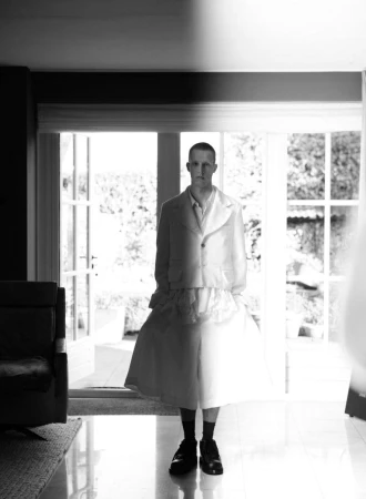 Model Jelle Huizinga standing in a white tailored jacket and wide culottes by French doors in a black and white portrait.