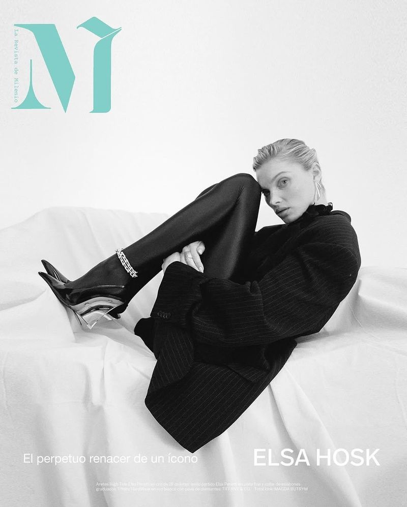 Fashion shot of Elsa Hosk on a white surface, wearing a black top and leggings, along with black high heels, and silver earring and bracelet.