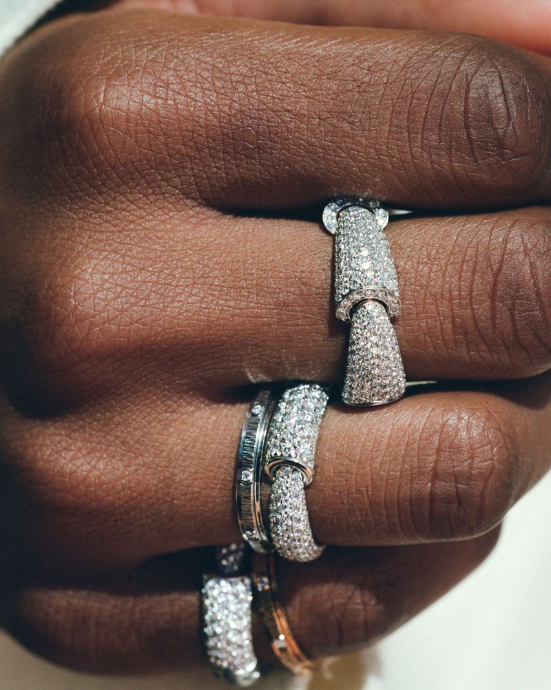 Close-up of fingers wearing jointed pavé diamond rings and white gold bands against a bright background.