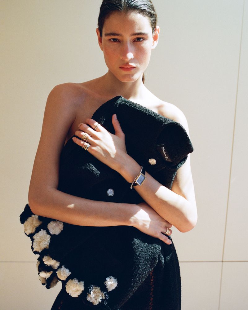 Model Luiza Perote clutching a black knit Chanel garment against a minimalist pale background.