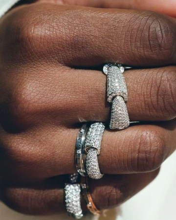Close-up of fingers wearing jointed pavé diamond rings and white gold bands against a bright background.