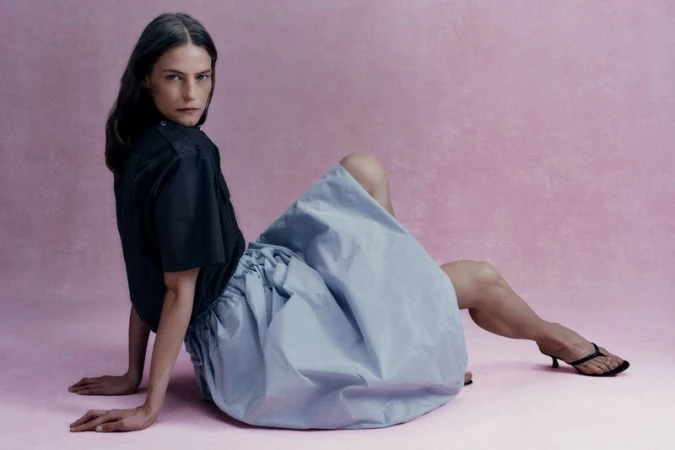 Model Viktorija Bauzyte seated on a pink studio floor wearing a black short-sleeve shirt and voluminous light blue puff skirt.