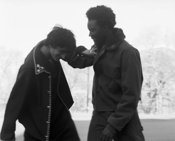 Black and white shot of two men laughing and interacting outdoors wearing dark jackets for The Greatest Magazine.