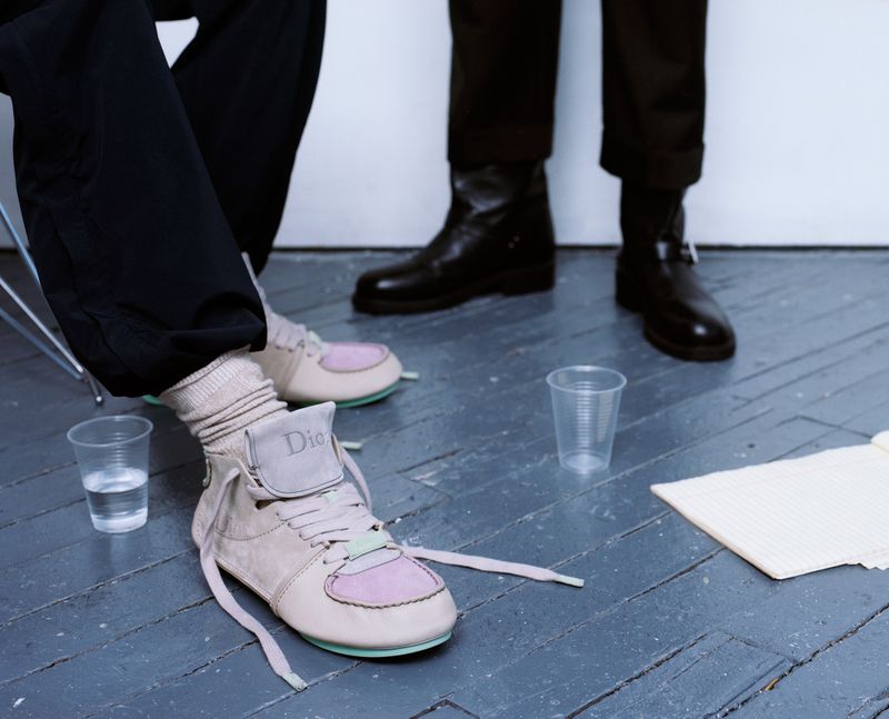 Close-up of pastel sneakers with ribbed socks alongside black leather boots on a painted wooden floor.