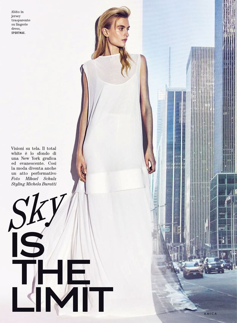 Model Veronika Vilim in a sleeveless white gown against a backdrop composited with a city skyscraper view.