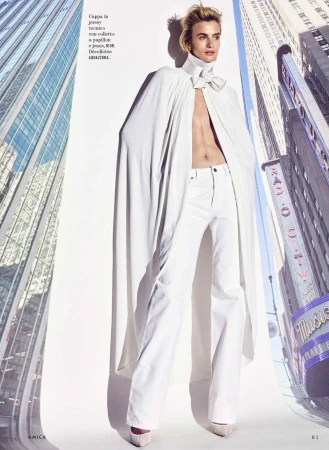 Model Veronika Vilim posing in an open white cape and matching white pants flanked by skyscraper backdrops.