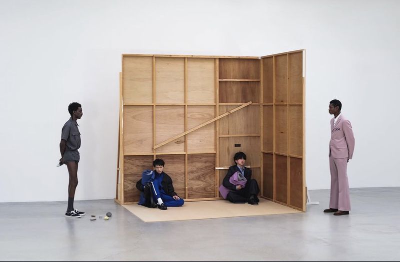 Four male models pose around a wooden partition structure inside a white studio space for Them Magazine editorial.