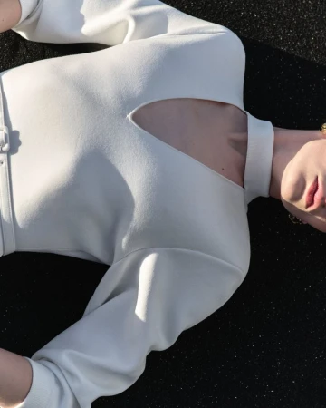 Model Anna Rud wearing an off-white structured cutout neckline top lying on a dark textured surface.