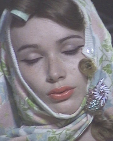 Close-up portrait of a woman with eyes closed wearing a floral pastel headscarf pinned with an ornate brooch.