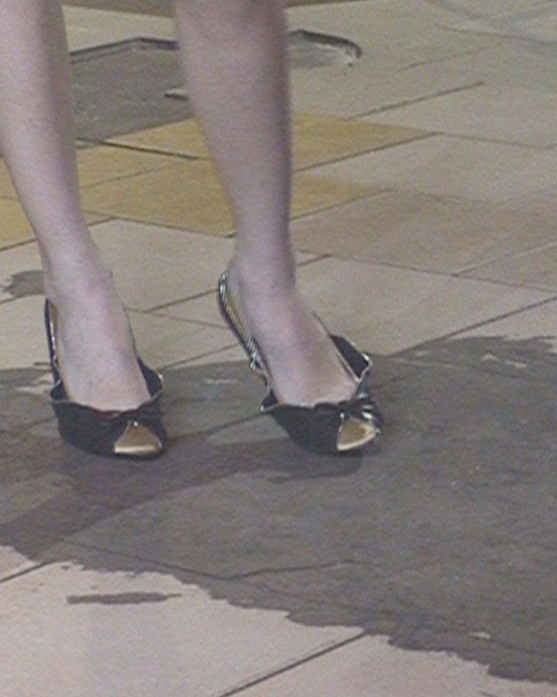 Close-up of a person's lower legs and feet wearing black peep-toe slingback heels on a tiled floor.