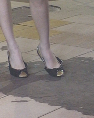 Close-up of a person's lower legs and feet wearing black peep-toe slingback heels on a tiled floor.