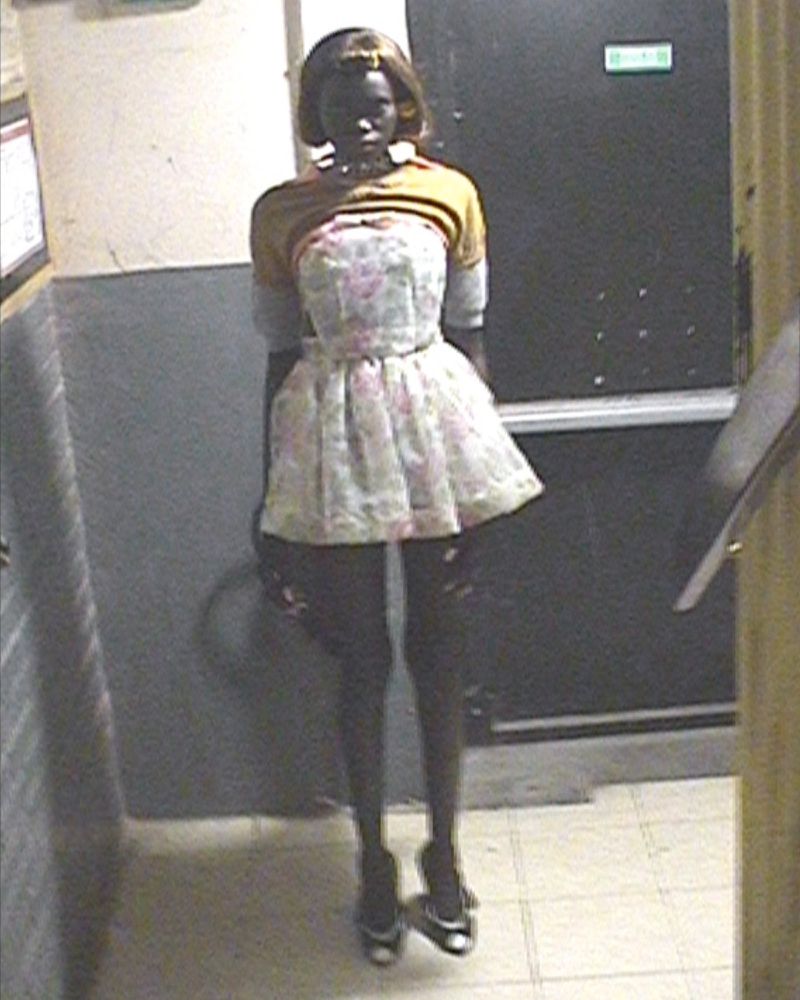 Fashion model in a floral mini dress and heels captured from a high angle security camera perspective in a hallway.