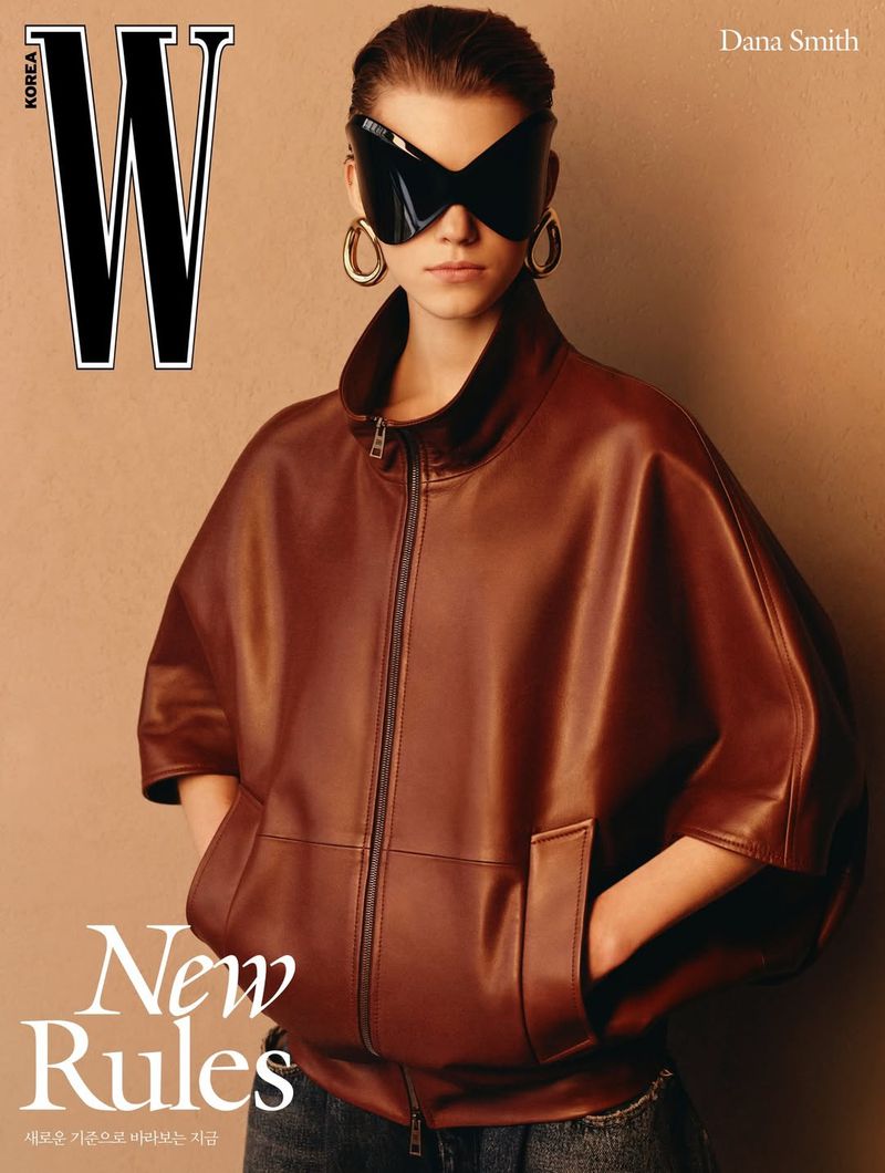 Model Dana Smith wearing an oversized brown leather cape jacket, sculptural black butterfly sunglasses, and chunky gold earrings.