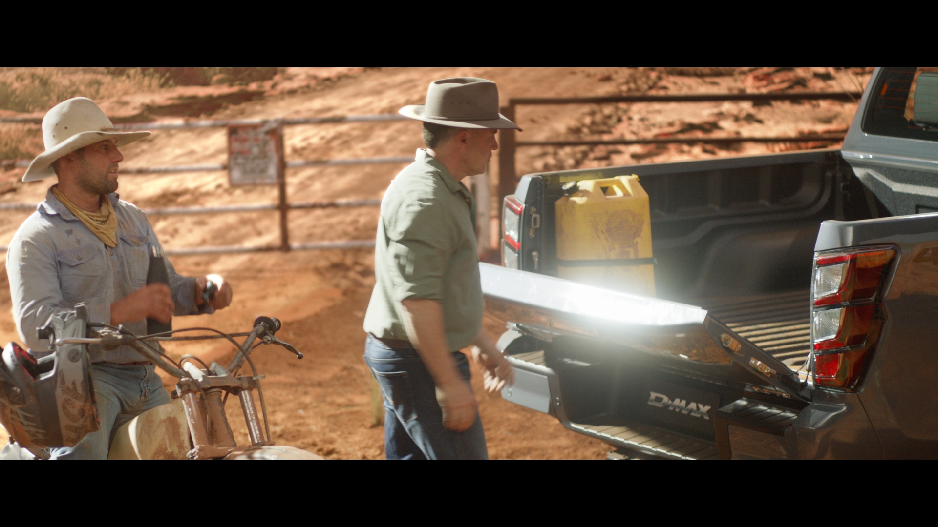 Two adult males near the back of a truck and a motorbike in a rural setting, wearing hats and casual clothing.