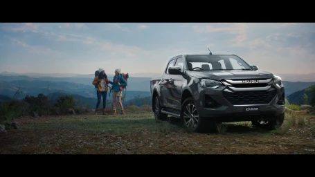 Dark pickup truck parked on a mountain overlook with two hikers standing in the background under an overcast sky.