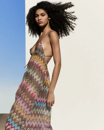 Woman posing in a colorful zig-zag dress against a blue and white background in a fashion shot, showcasing the dress and her curly hair.
